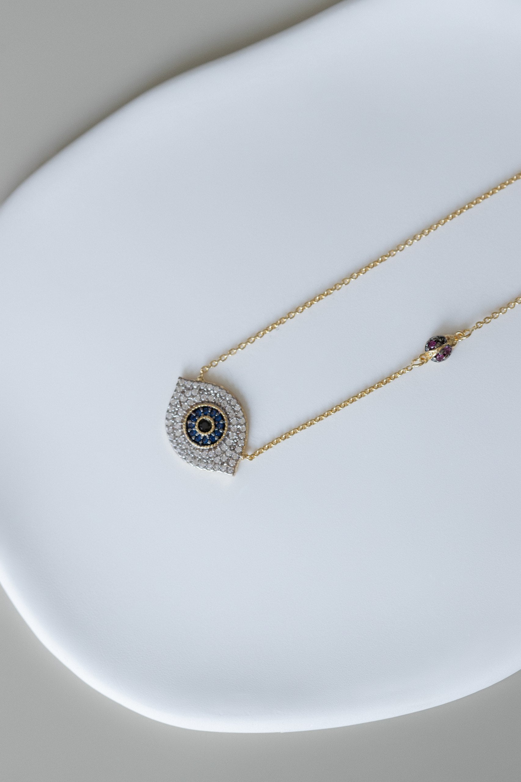 A delicate necklace featuring an evil eye pendant adorned with micro zircons, symbolizing protection and positivity. Accented with a charming &nbsp;ladybug detail, it combines elegance and good fortune in a timeless design.