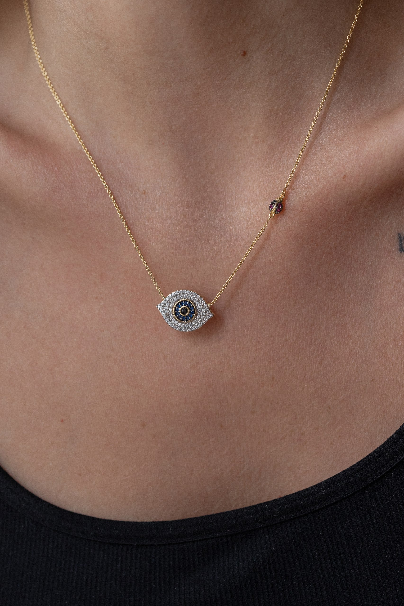 A delicate necklace featuring an evil eye pendant adorned with micro zircons, symbolizing protection and positivity. Accented with a charming &nbsp;ladybug detail, it combines elegance and good fortune in a timeless design.